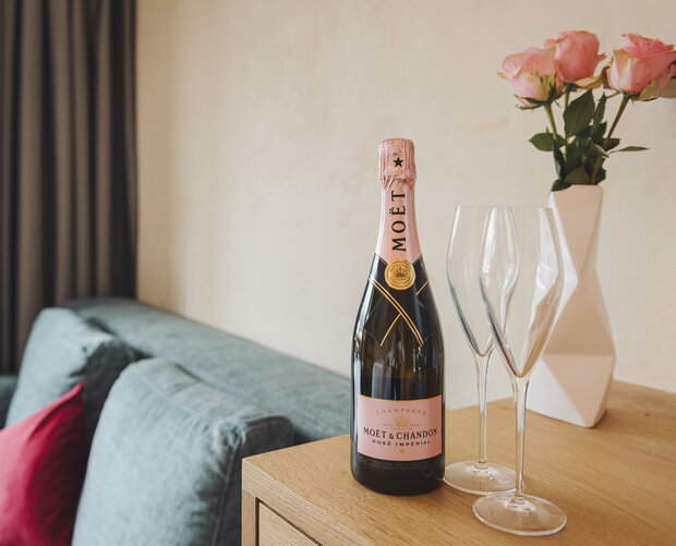 Flasche Sekt mit Strauß Rosen und Couch