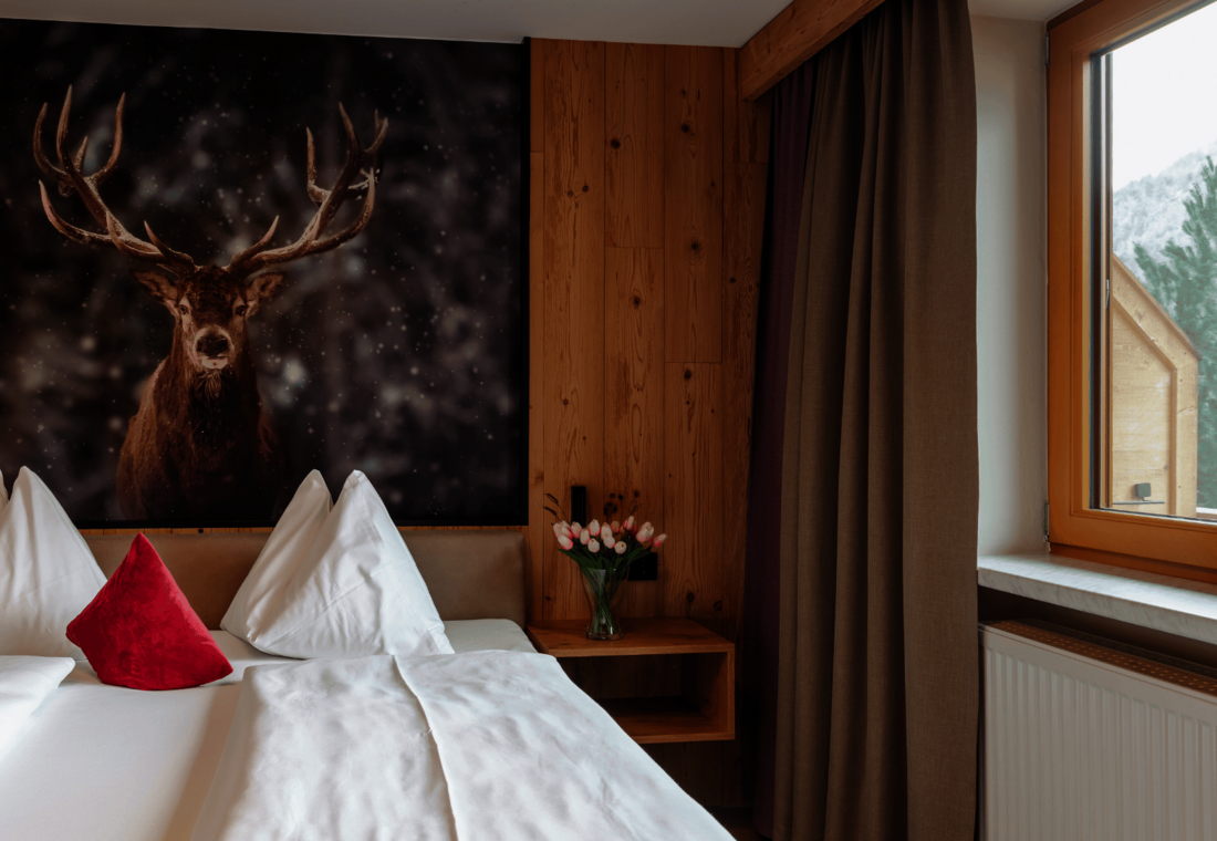 Doppelbett mit Hirsch an der Wand und Nachttisch