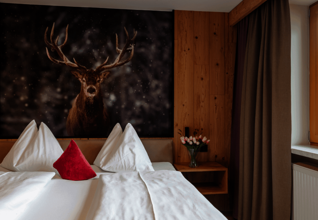 Gemütliches Doppelzimmer mit Naturholzverkleidung und Hirschmotiv über dem Bett