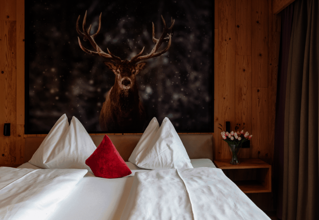 Gemütliches Doppelzimmer mit Naturholzverkleidung und Hirschmotiv über dem Bett