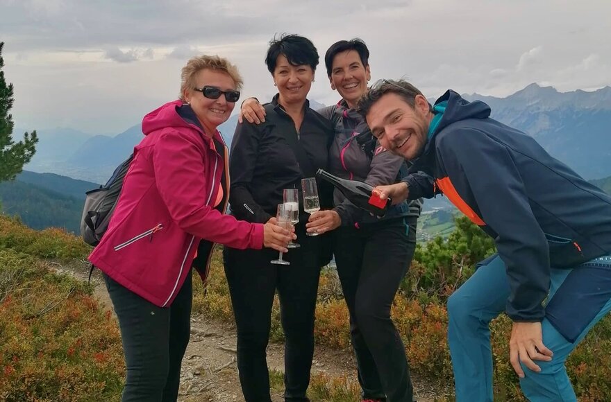Vier Menschen stoßen mit einer Flasche Sekt an in den Bergen