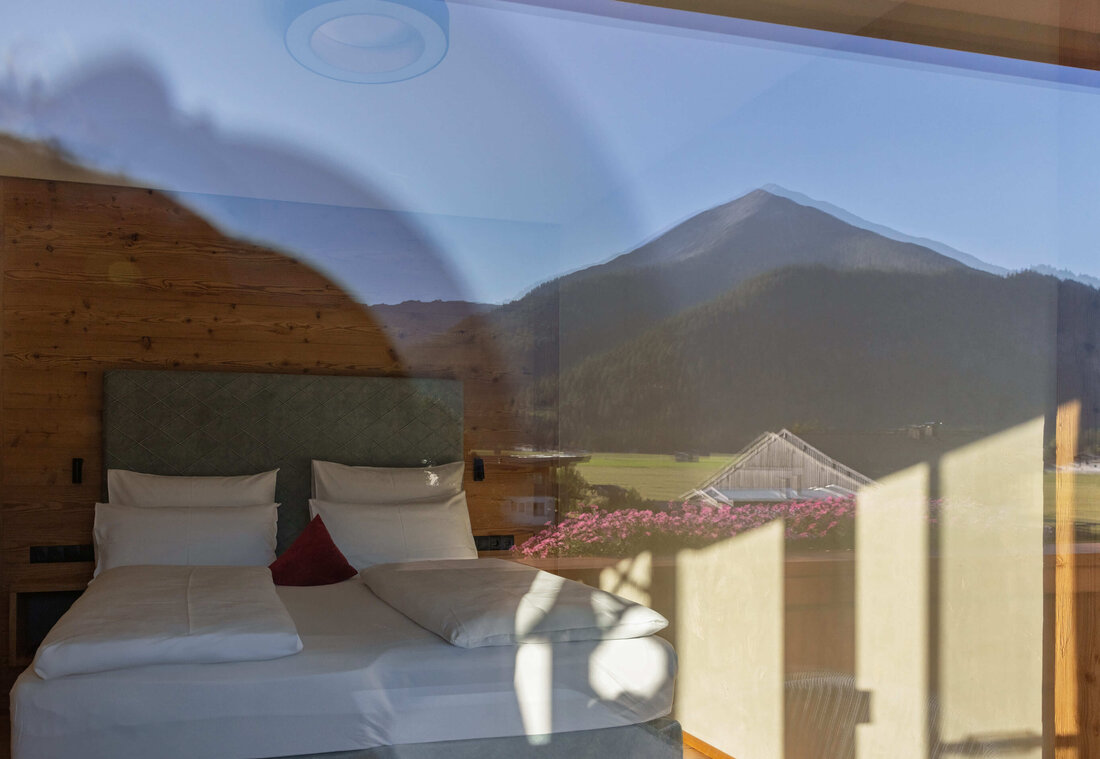 Großes Doppelbett mit Spiegelung der Berge und Blumen
