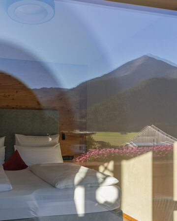 Großes Doppelbett mit Spiegelung der Berge und Blumen
